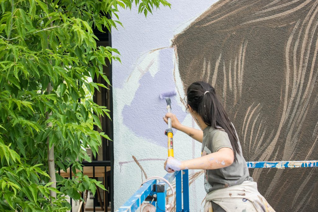 Tima en train de peindre au rouleau au festival Mural